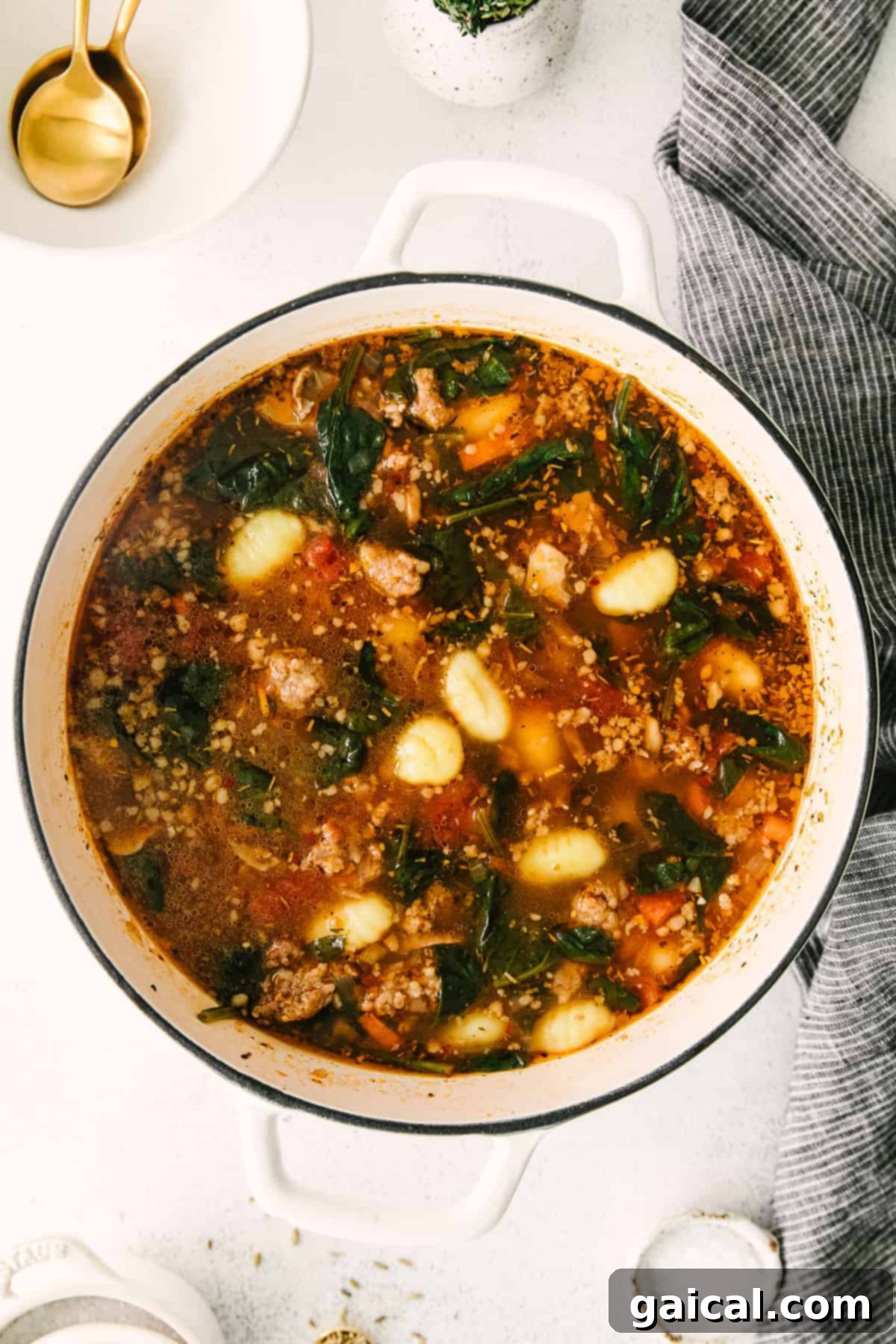 Sausage gnocchi soup in a stock pot, with gnocchi clearly visible and starting to float to the top, indicating they are cooked.