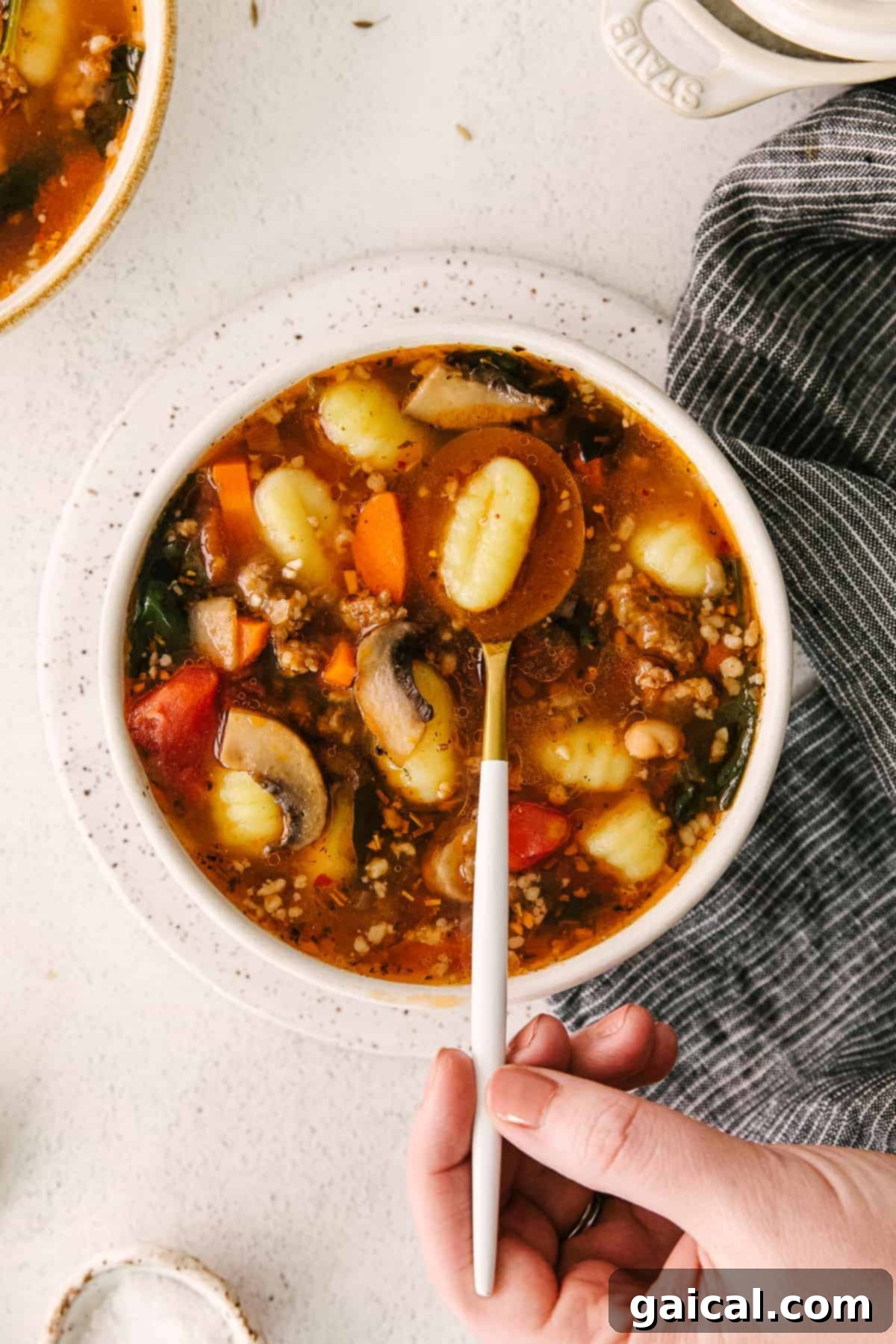 A close-up shot of a bowl of sausage gnocchi soup with a single gnocchi on a spoon, ready to be eaten.