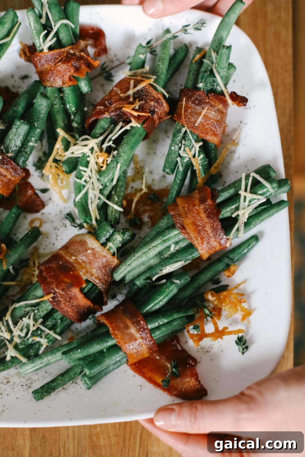 Gourmet Bacon Wrapped Green Beans with Parmesan Beautifully arranged bacon wrapped green beans on a white plate, garnished with shredded Parmesan cheese and fresh herbs, ready to be served.