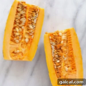 Two halves of delicata squash, perfectly de-seeded and ready for slicing, resting on a marble surface.
