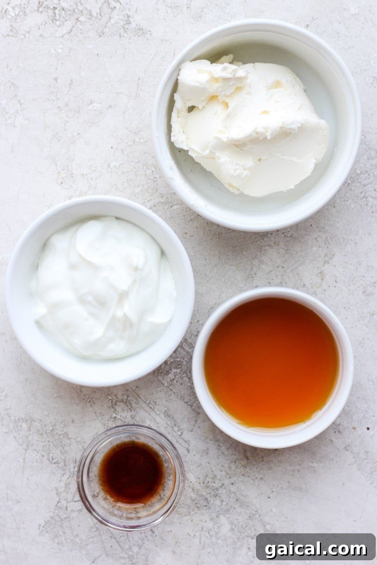 Guilt-Free Cream Cheese Frosting 3 Four individual bowls displaying the simple yet essential ingredients for healthy cream cheese frosting: softened cream cheese, plain nonfat Greek yogurt, pure maple syrup, and clear vanilla extract.