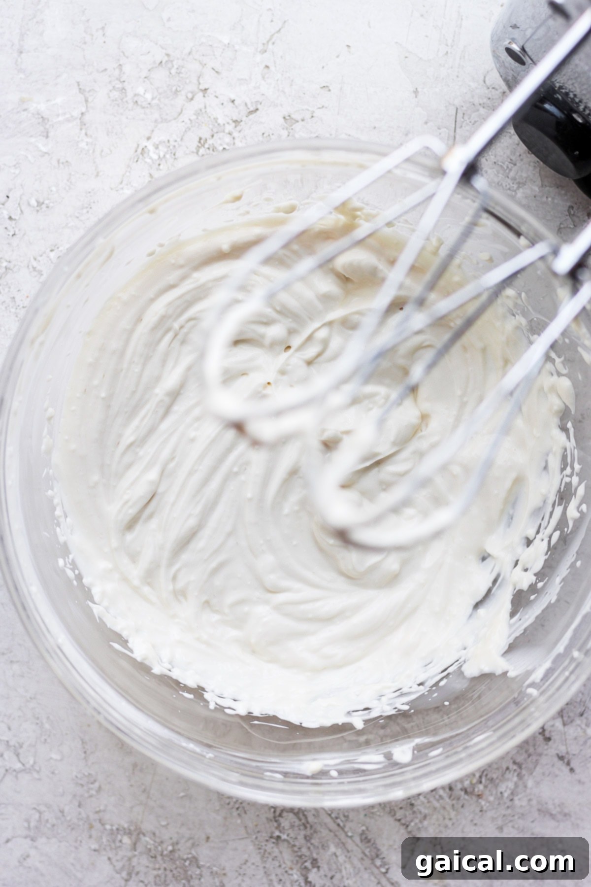 Guilt-Free Cream Cheese Frosting 6 An electric hand mixer actively blending healthy cream cheese frosting in a large mixing bowl, showcasing the transformation into a smooth and creamy texture.