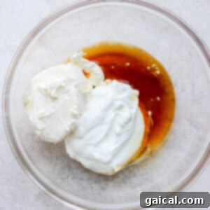 All four ingredients for healthy cream cheese frosting – softened fat-free cream cheese, plain nonfat Greek yogurt, pure maple syrup, and vanilla extract – gathered in a large mixing bowl, ready for blending.