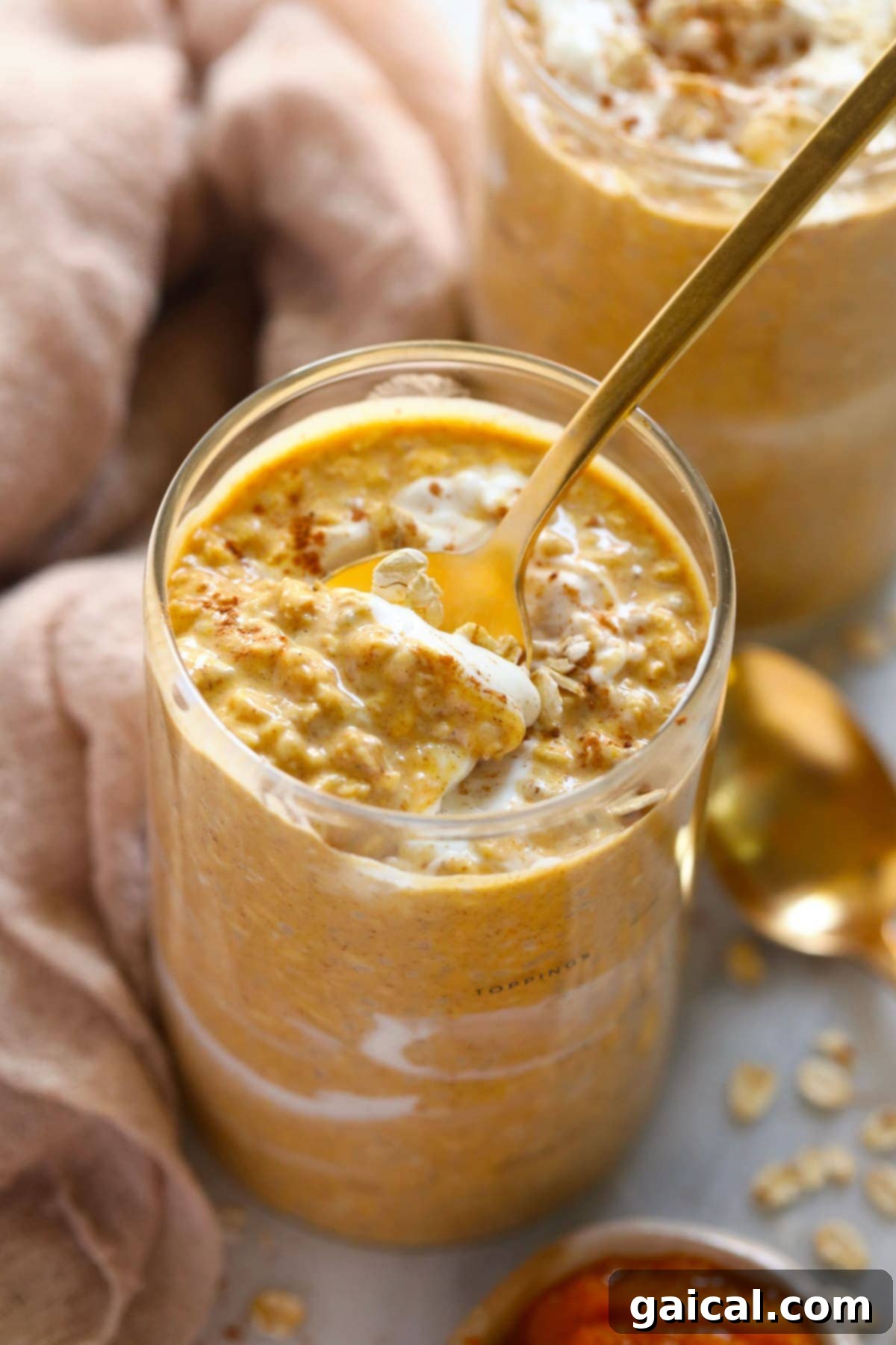 A spoon digging into a jar of Pumpkin Cheesecake Overnight Oats, showing the creamy texture.
