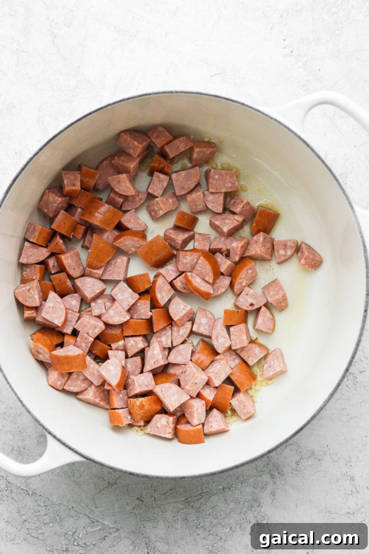 Sliced andouille sausage browning in a Dutch oven with olive oil