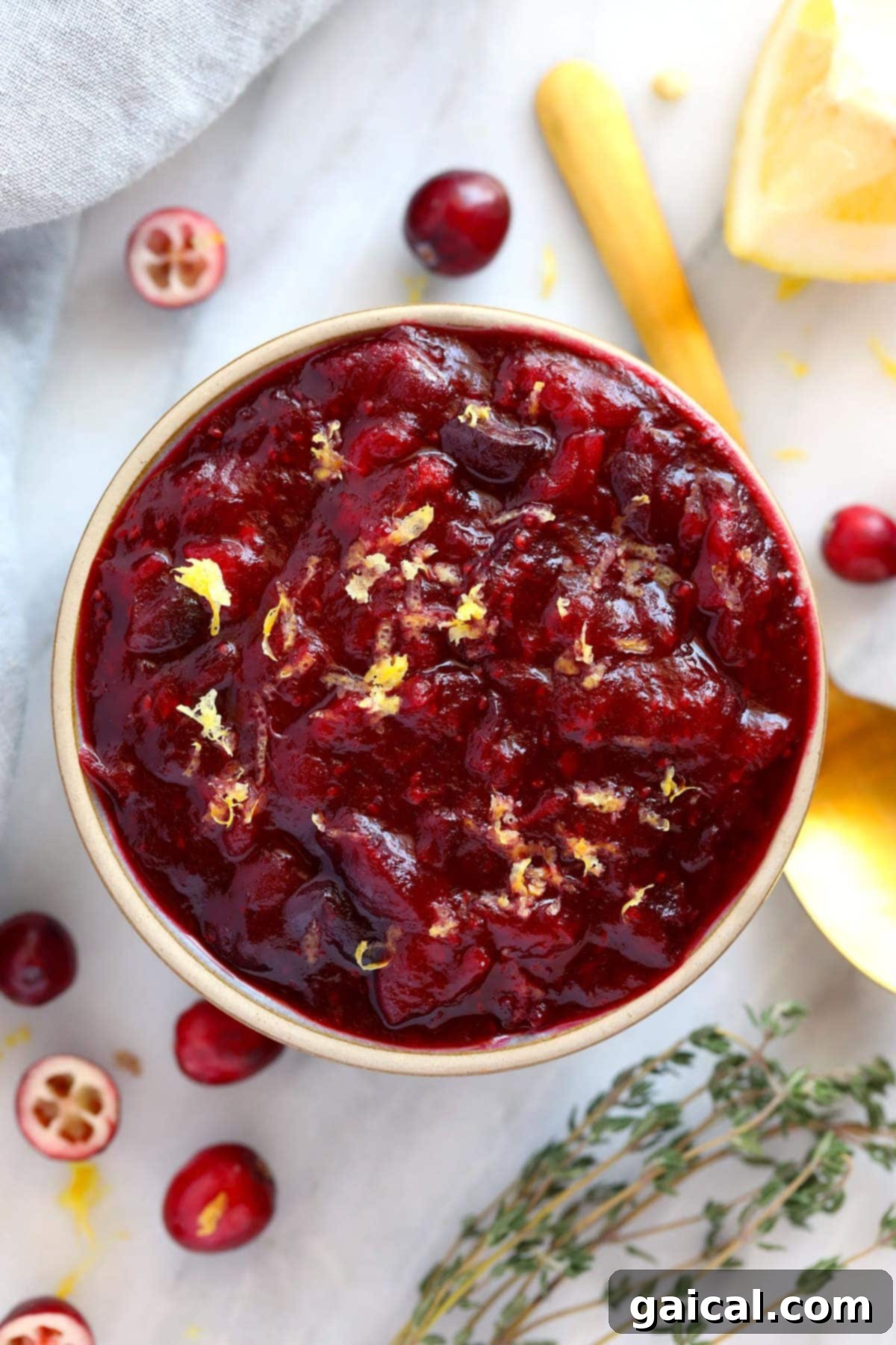 A bowl of vibrant homemade lemon ginger cranberry sauce, garnished with fresh lemon slices and a sprig of thyme, ready to serve.