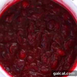 Homemade lemon ginger cranberry sauce simmering and thickening in a saucepan on the stove.