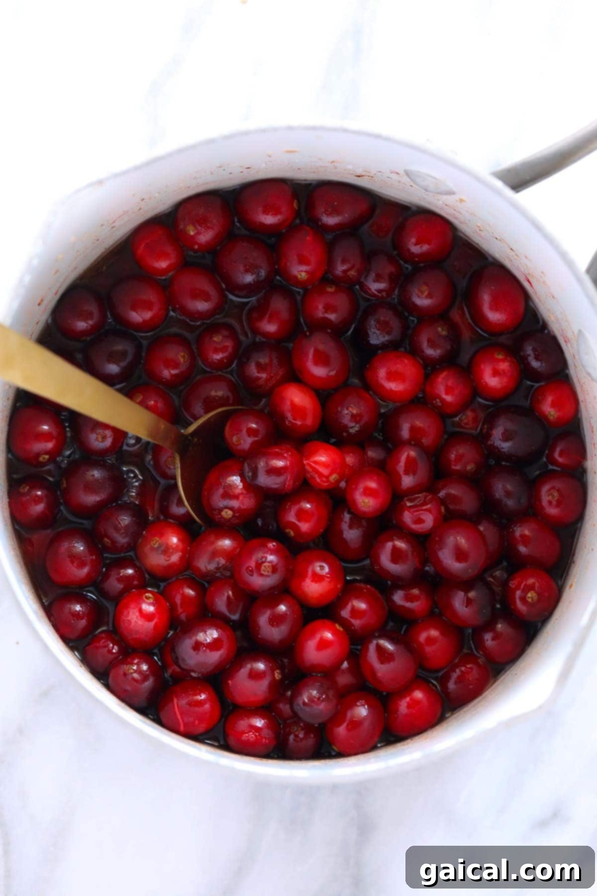 Fresh, vibrant red cranberries simmering in a saucepan on the stovetop, beginning to break down and form a sauce.