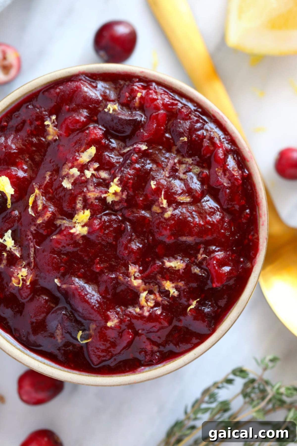 A serving of homemade lemon ginger cranberry sauce in a white bowl, garnished with a sprig of thyme and a lemon slice.
