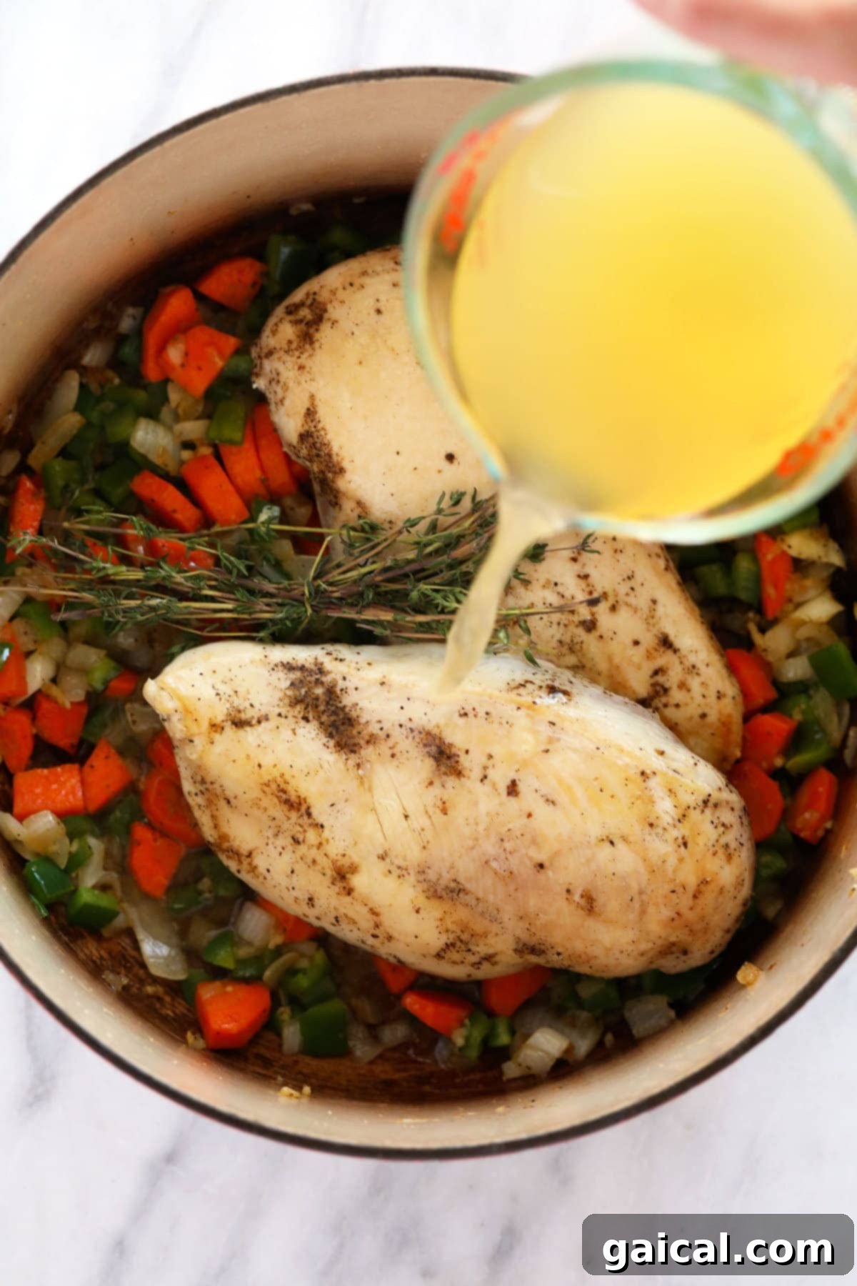 Hearty Chicken Wild Rice Soup 6 Broth being poured over chicken breasts, carrots, and other aromatics in a large pot for chicken wild rice soup.