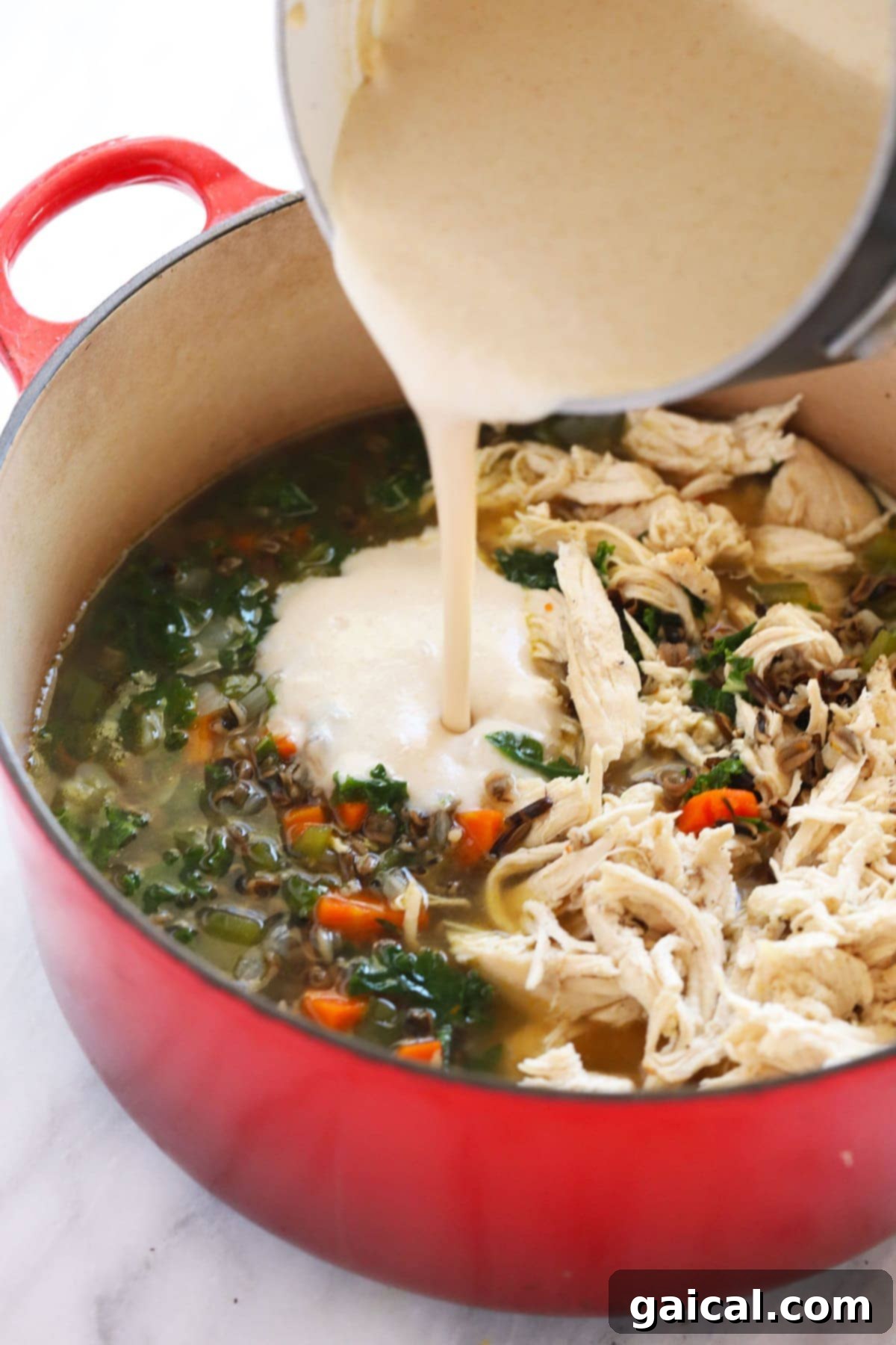 Hearty Chicken Wild Rice Soup 7 A stream of creamy roux being poured into the simmering chicken wild rice soup.