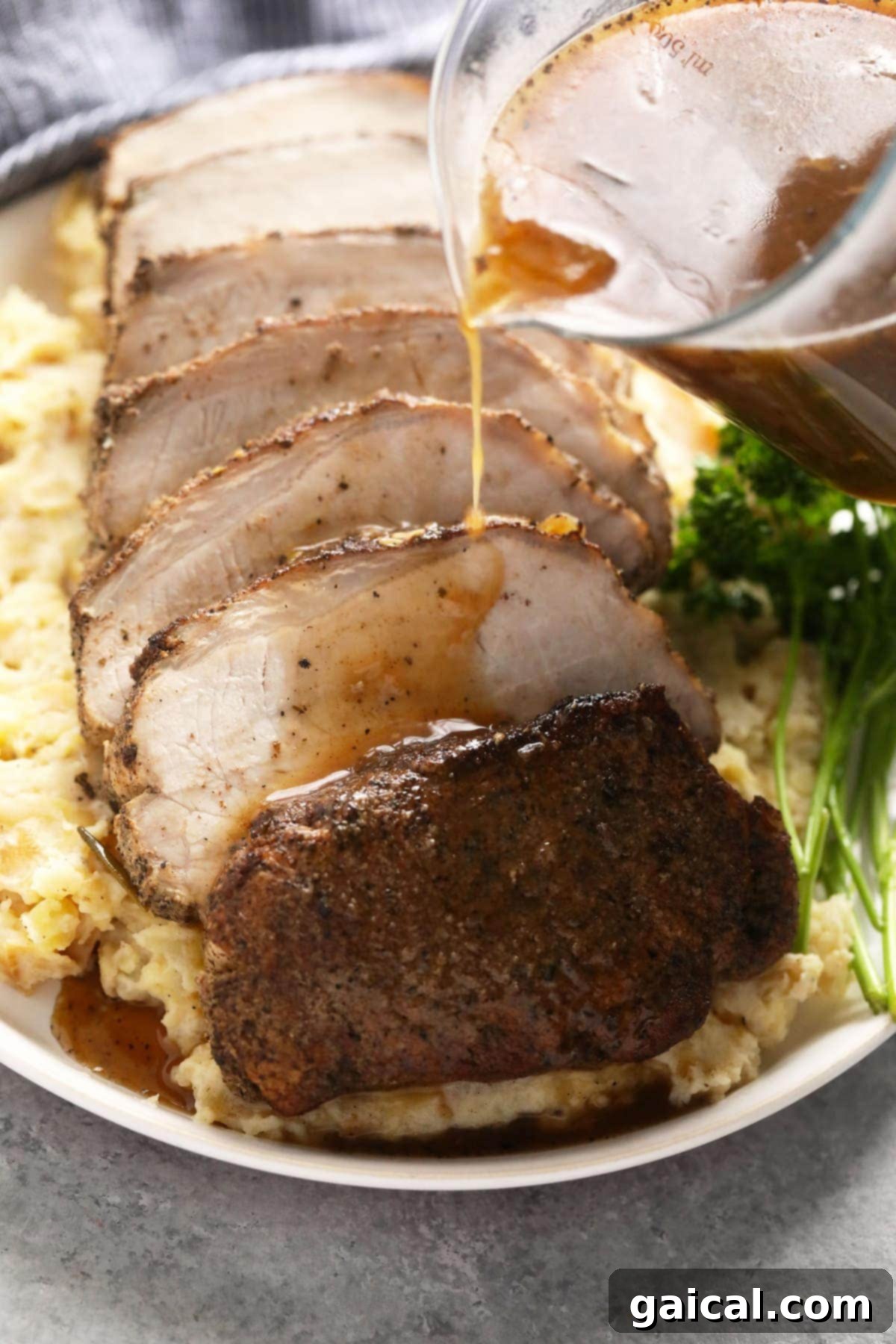 This is the most tender Slow Cooker Pork Loin roast recipe ever! It's served with potatoes and a savory gravy for the perfect meal. Enjoy! slow cooker pork loin sliced on a bed of mashed potatoes, drizzled with savory gravy.