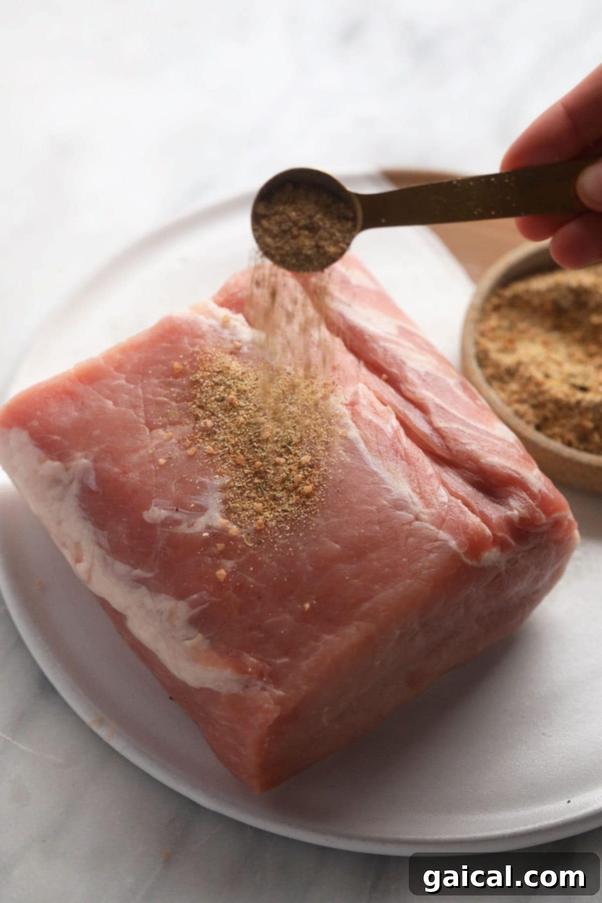 This is the most tender Slow Cooker Pork Loin roast recipe ever! It's served with potatoes and a savory gravy for the perfect meal. Enjoy! raw pork loin roast being seasoned generously with a pork dry rub before searing.