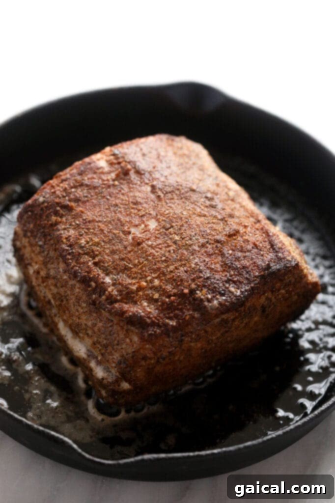 This is the most tender Slow Cooker Pork Loin roast recipe ever! It's served with potatoes and a savory gravy for the perfect meal. Enjoy! slow cooker pork loin being seared to perfection in a cast iron skillet, creating a delicious crust.