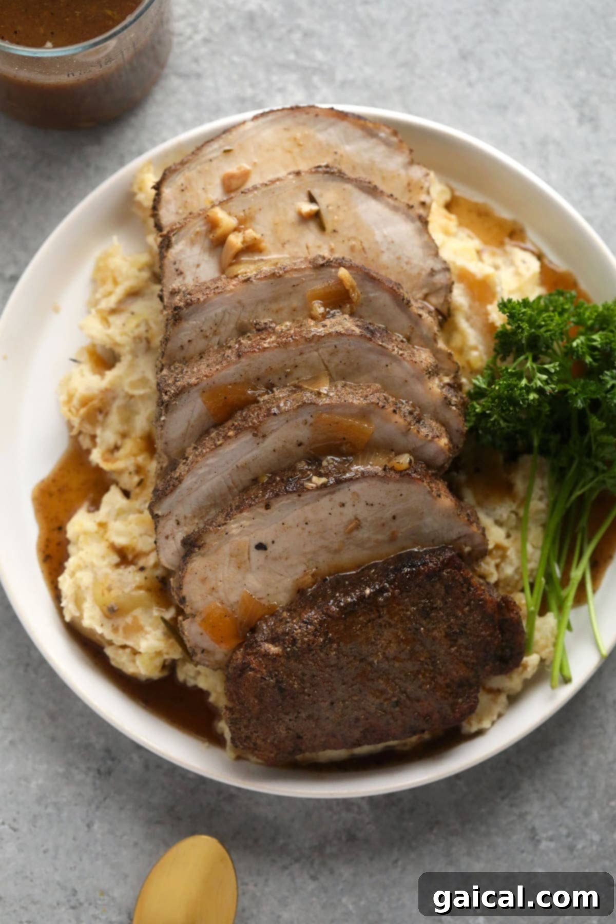 This is the most tender Slow Cooker Pork Loin roast recipe ever! It's served with potatoes and a savory gravy for the perfect meal. Enjoy! slow cooker pork loin on a bed of mashed potatoes covered in delicious homemade gravy, ready to serve.
