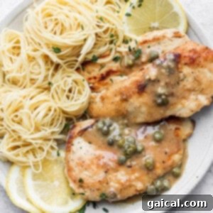 Chicken piccata on a plate with angel hair pasta and lemon slices.