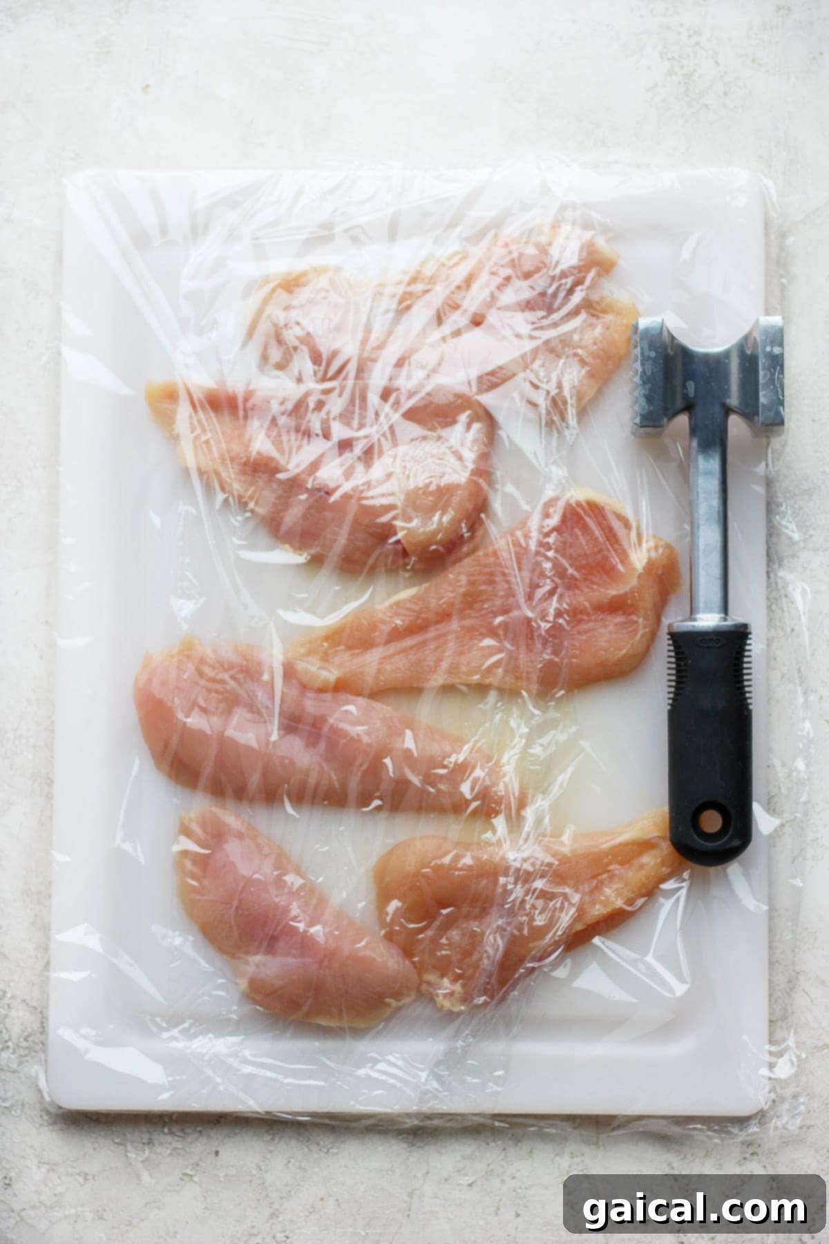 Pounding chicken breast on a cutting board with a meat cleaver to even thickness for chicken piccata.