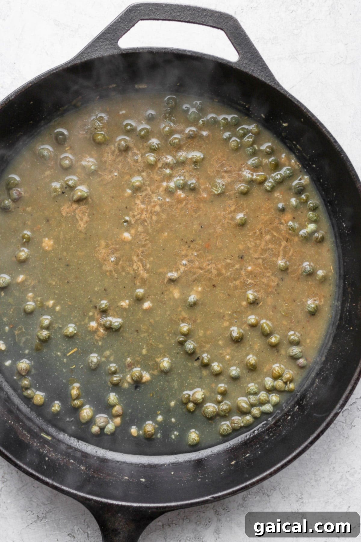 Luscious white wine lemon caper sauce simmering in a cast iron skillet for chicken piccata.