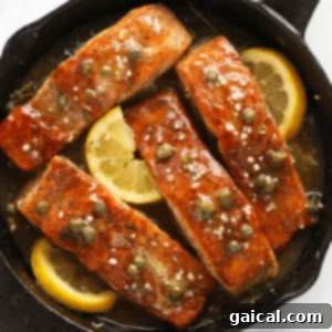 Perfectly seared salmon fillets in a skillet, garnished with fresh lemon slices and herbs.