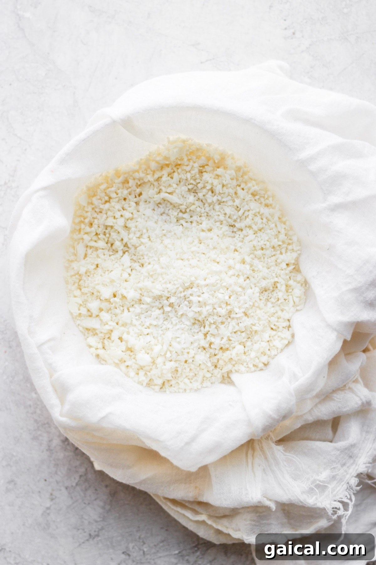 Finely processed cauliflower rice being squeezed in a tea towel to remove excess moisture, a critical step for a crispy crust.