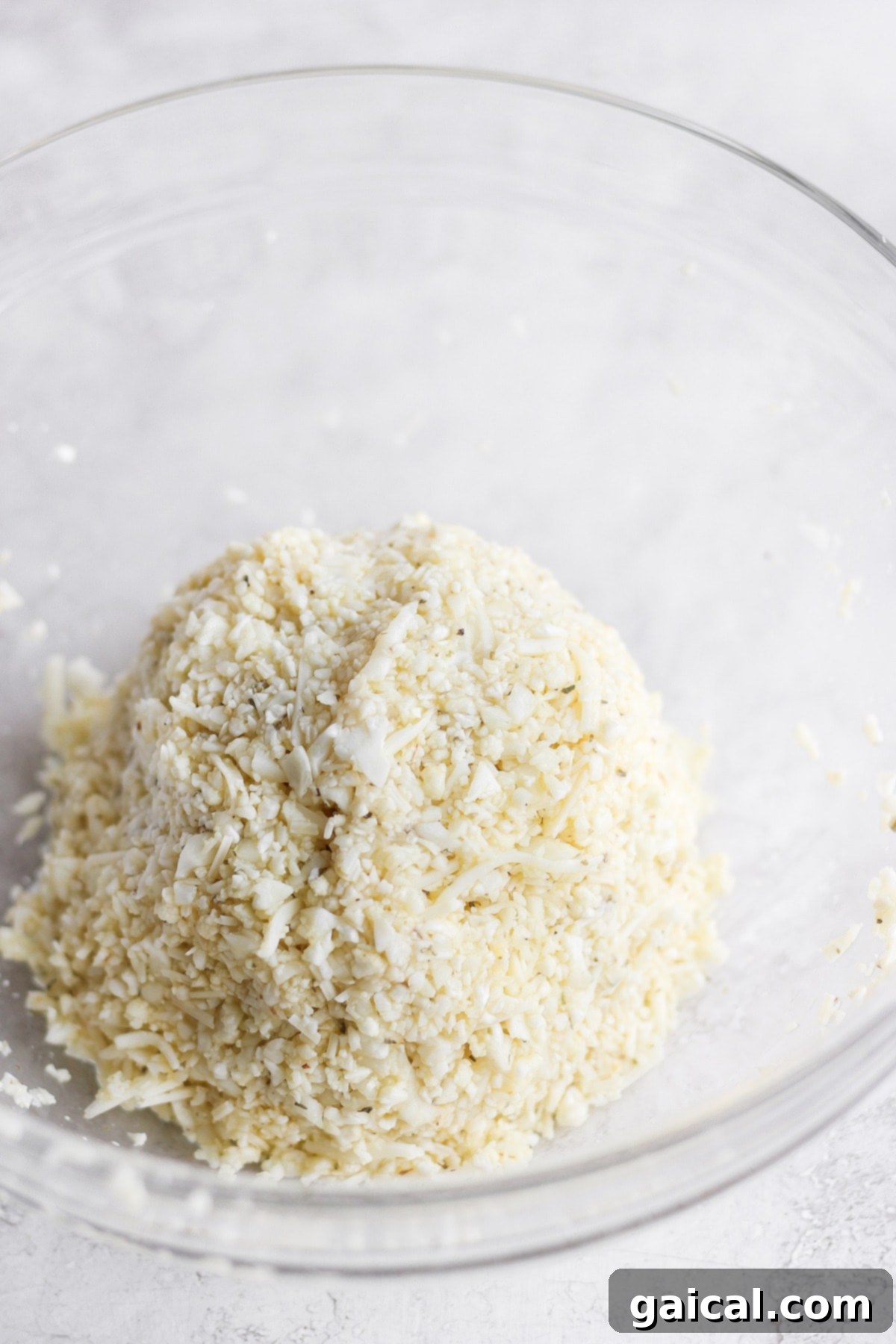 Cauliflower pizza dough shaped into a compact ball, demonstrating its cohesive form before being pressed onto the baking sheet.