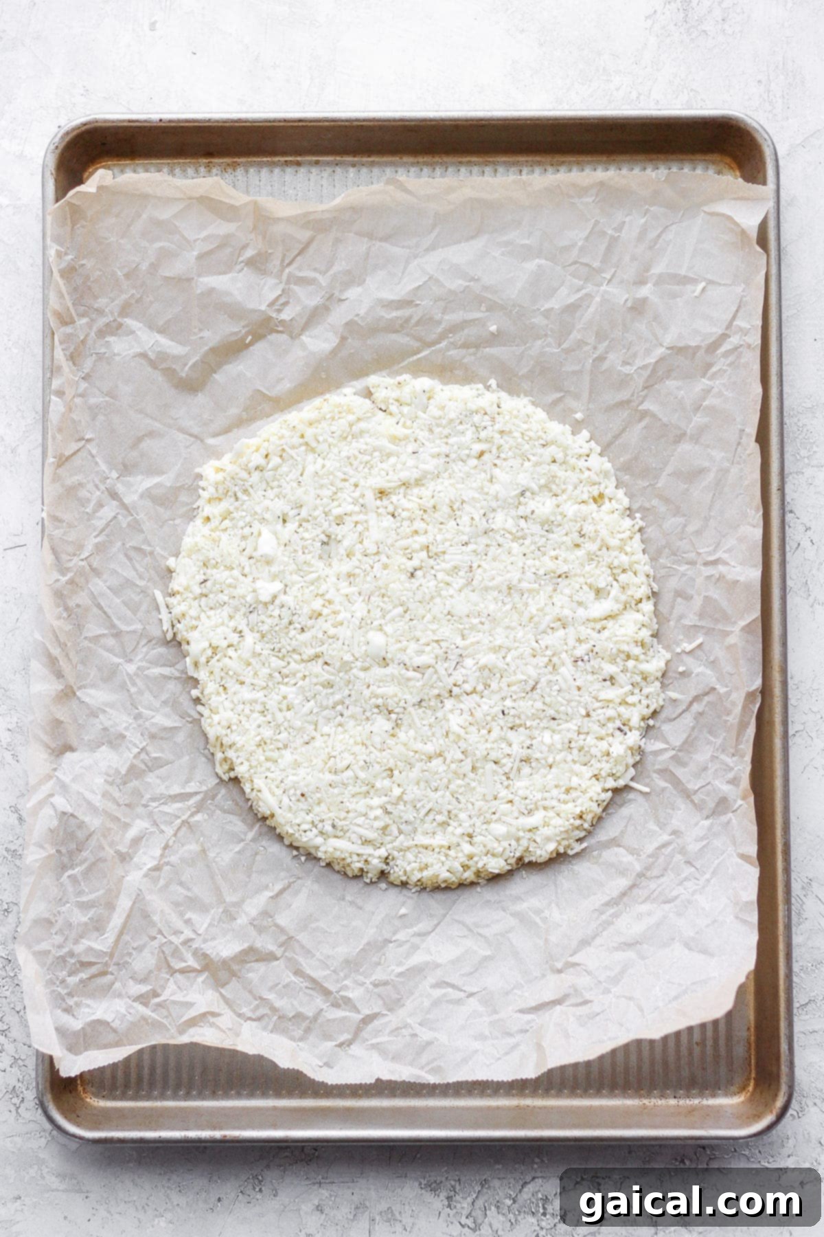 Cauliflower pizza crust perfectly shaped into a circle on parchment paper on a baking sheet, ready to go into the oven.