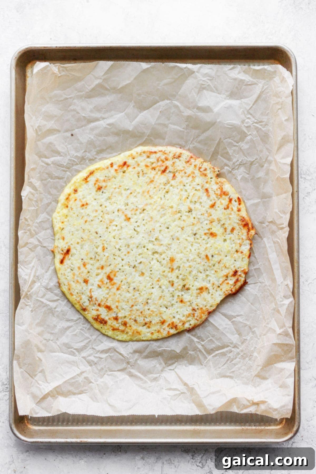 Golden brown cauliflower pizza crust cooling on parchment paper after being flipped and fully baked, ready for toppings.