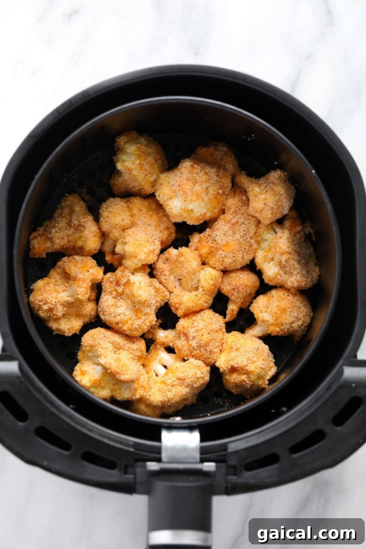 Crispy air fryer cauliflower florets cooking inside an air fryer basket, turning golden brown.