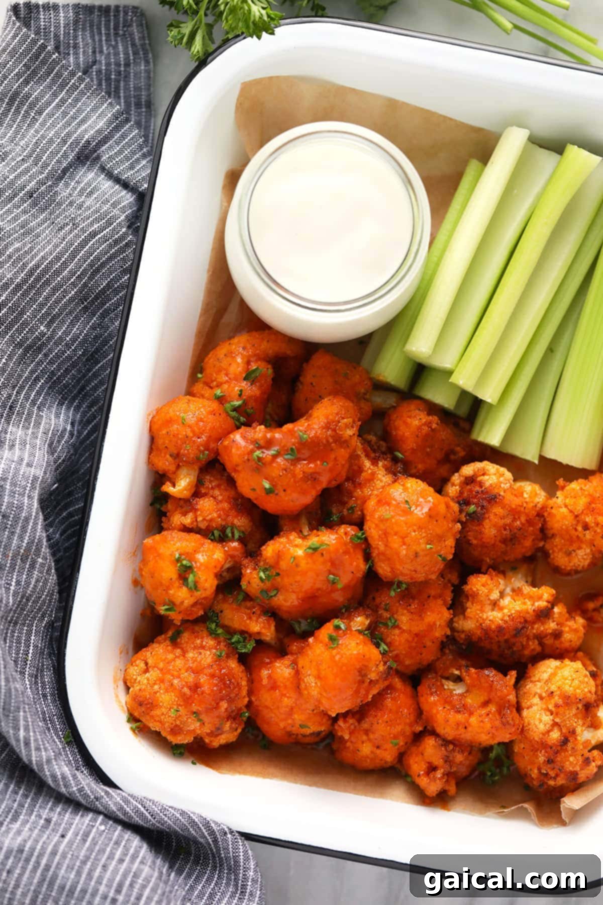 Air fryer buffalo cauliflower wings arranged in a container with a side of blue cheese dip and celery sticks.
