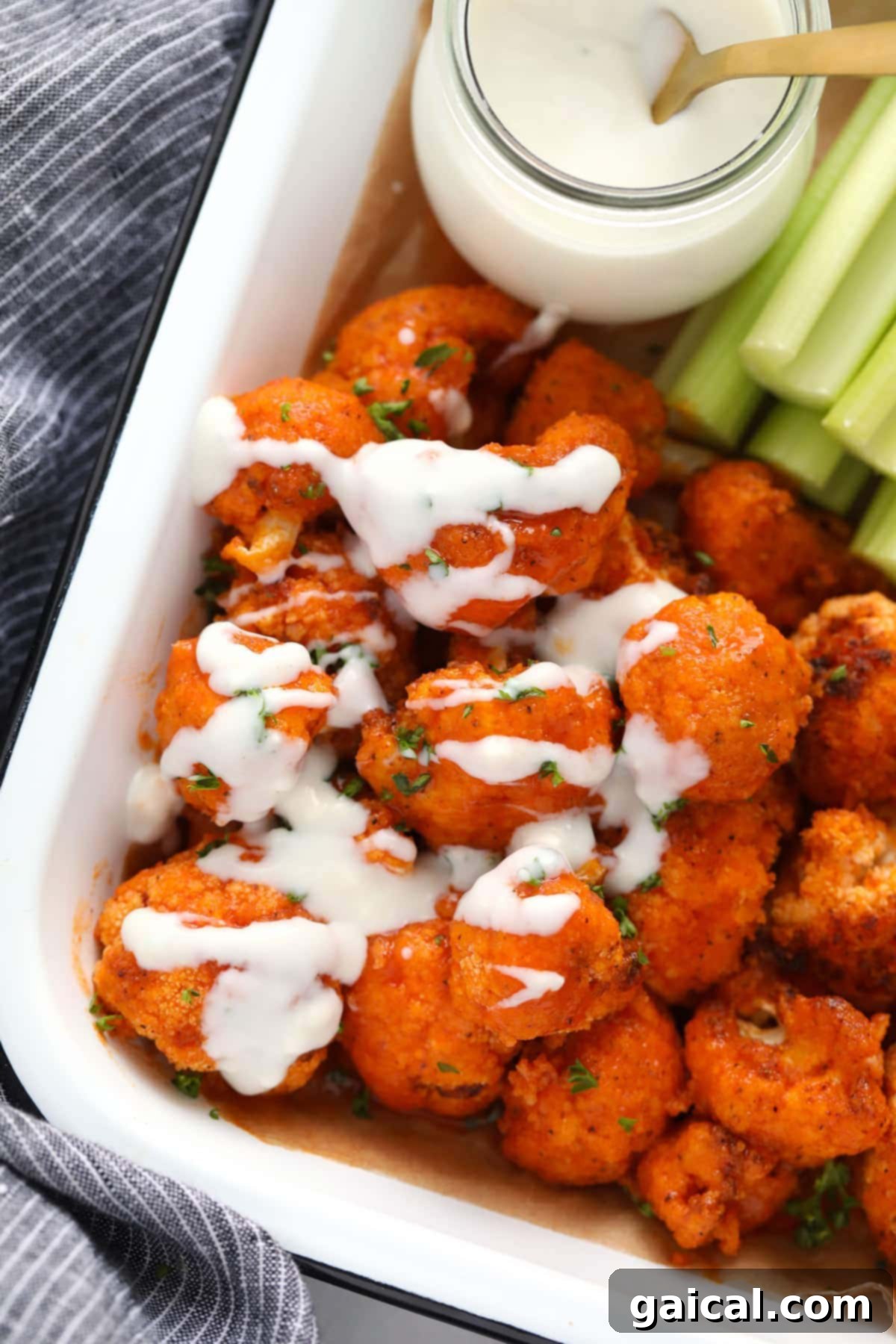 Blue cheese sauce generously drizzled over a platter of air fryer buffalo cauliflower wings, garnished for serving.