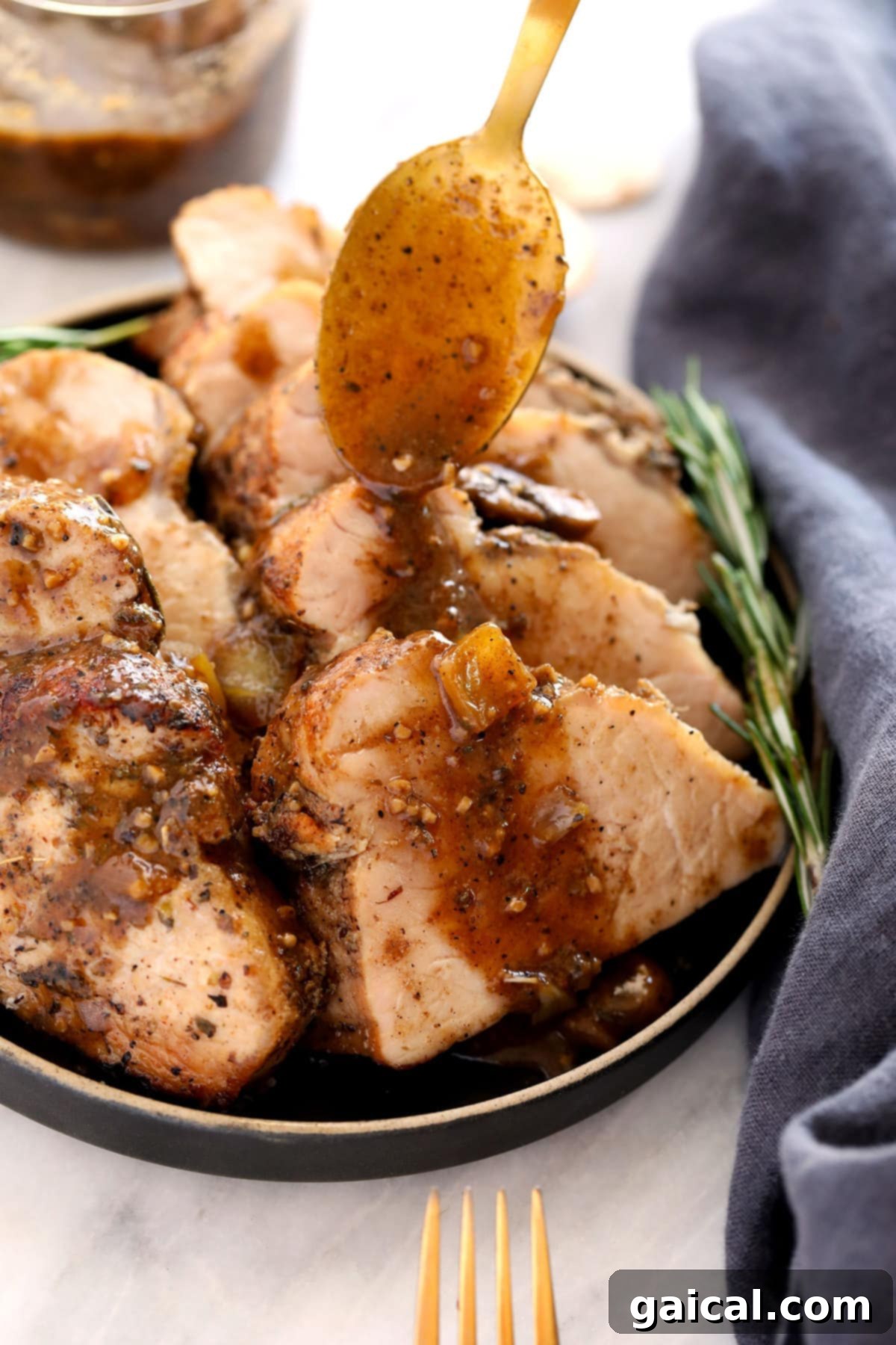 Baked pork tenderloin being drizzled with rich mushroom gravy in a cast iron skillet.