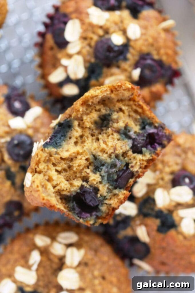 A blueberry oatmeal muffin perfectly cut in half, revealing its fluffy interior and an abundance of plump, juicy blueberries.