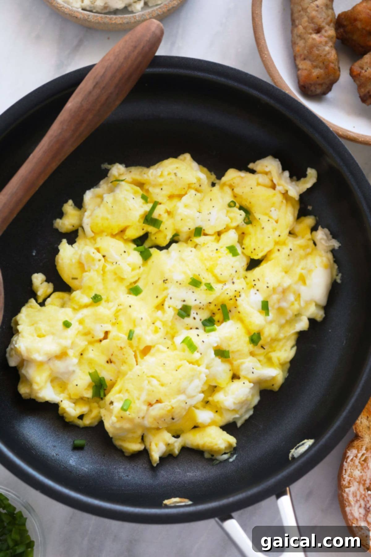 Fluffy Scrambled Eggs with Chives A close-up of perfectly cooked scrambled eggs, delicately garnished with fresh chopped chives, presented in a black skillet.