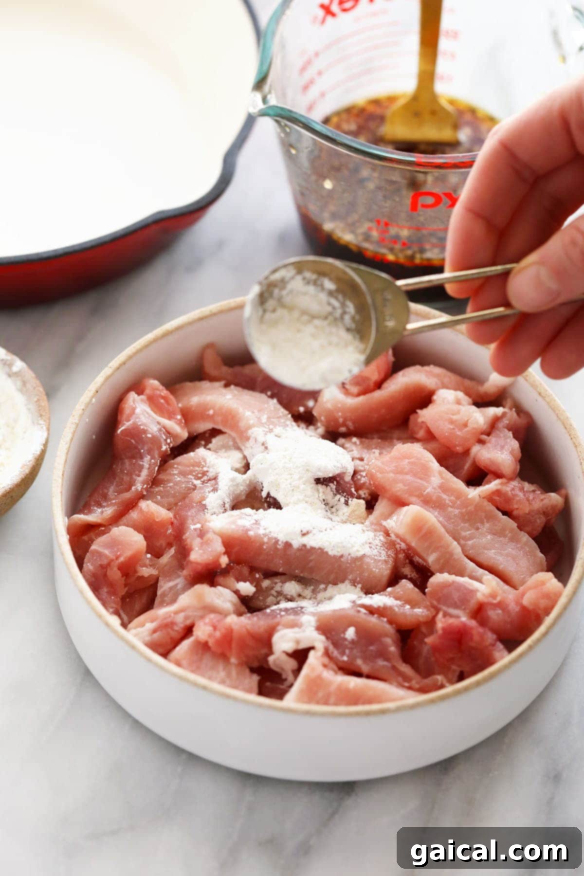 Coating Pork with Cornstarch for Crispiness Pork strips being sprinkled with cornstarch before cooking, ensuring a crispy texture.