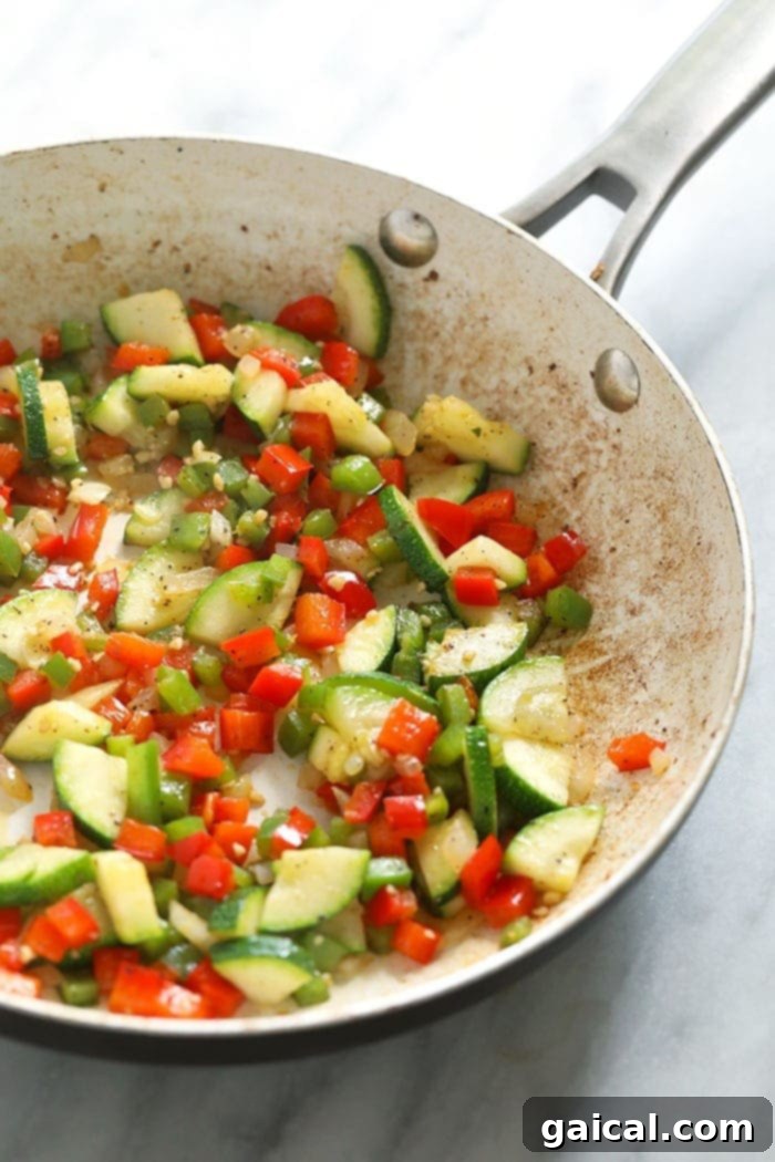 Pre-cook your vegetables with farm-fresh eggs and a sprinkle of parmesan cheese for a low-carb breakfast option! Vibrant, fresh vegetables like bell peppers, onions, and zucchini sautéing in olive oil in a non-stick pan on the stovetop, before being combined with eggs for a frittata.