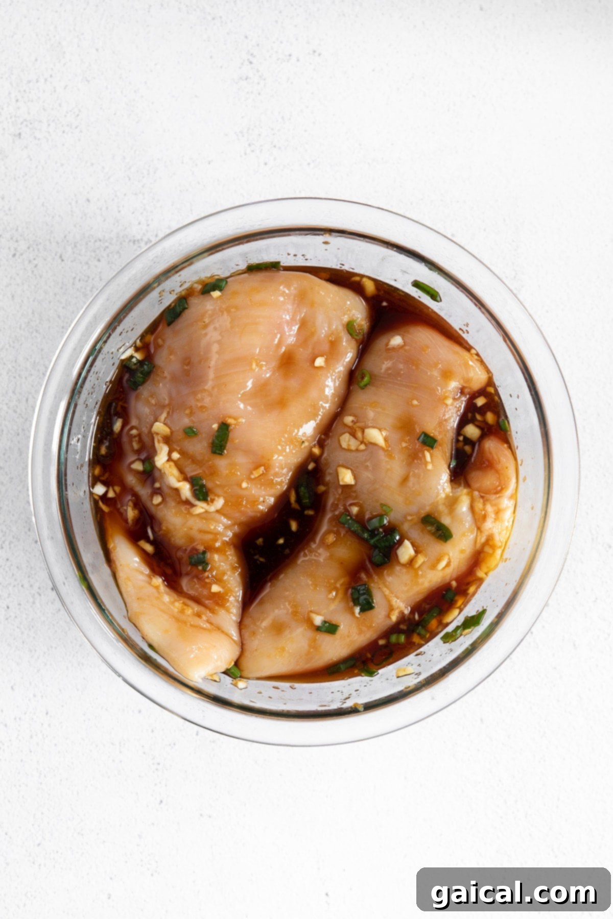 Seriously delicious baked teriyaki chicken breast comes together with easy-to-find ingredients. This teriyaki chicken comes out so tender and saucy! Raw chicken breast marinating in a glass bowl filled with rich teriyaki sauce.