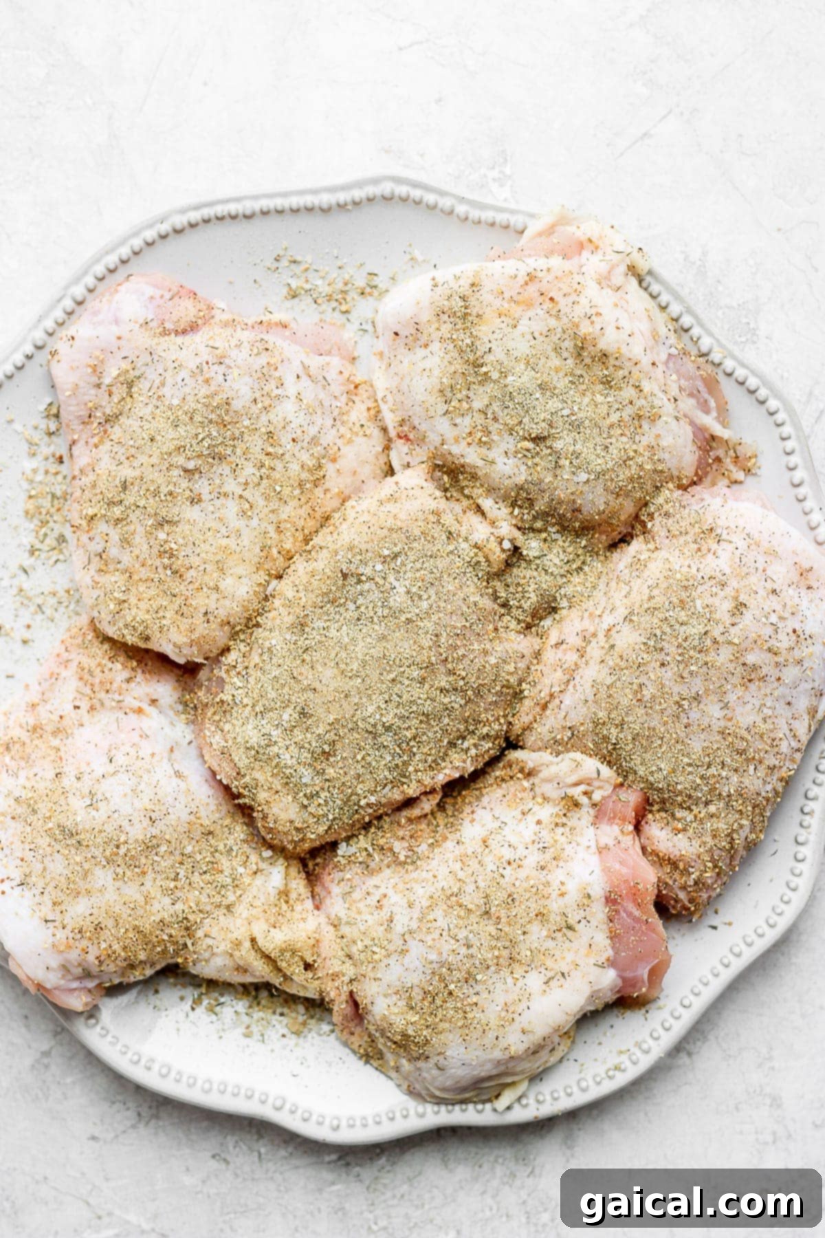 Seasoned bone-in chicken thighs on a plate, ready to be seared in a Dutch oven.