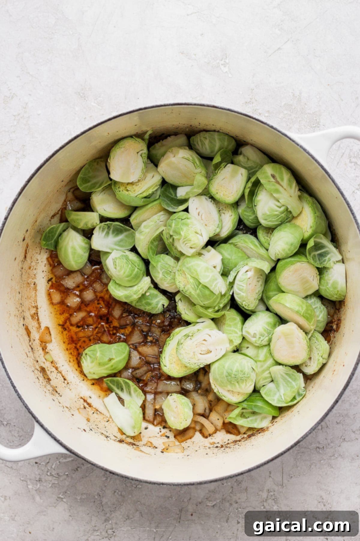 Uncooked Brussels sprouts and onion being sautéed in a Dutch oven, building the dish's flavor base.