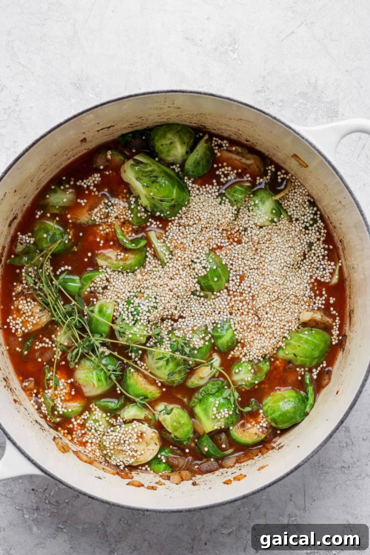 Brussels sprouts, uncooked quinoa, and chicken broth in a Dutch oven, topped with seared chicken thighs before baking.