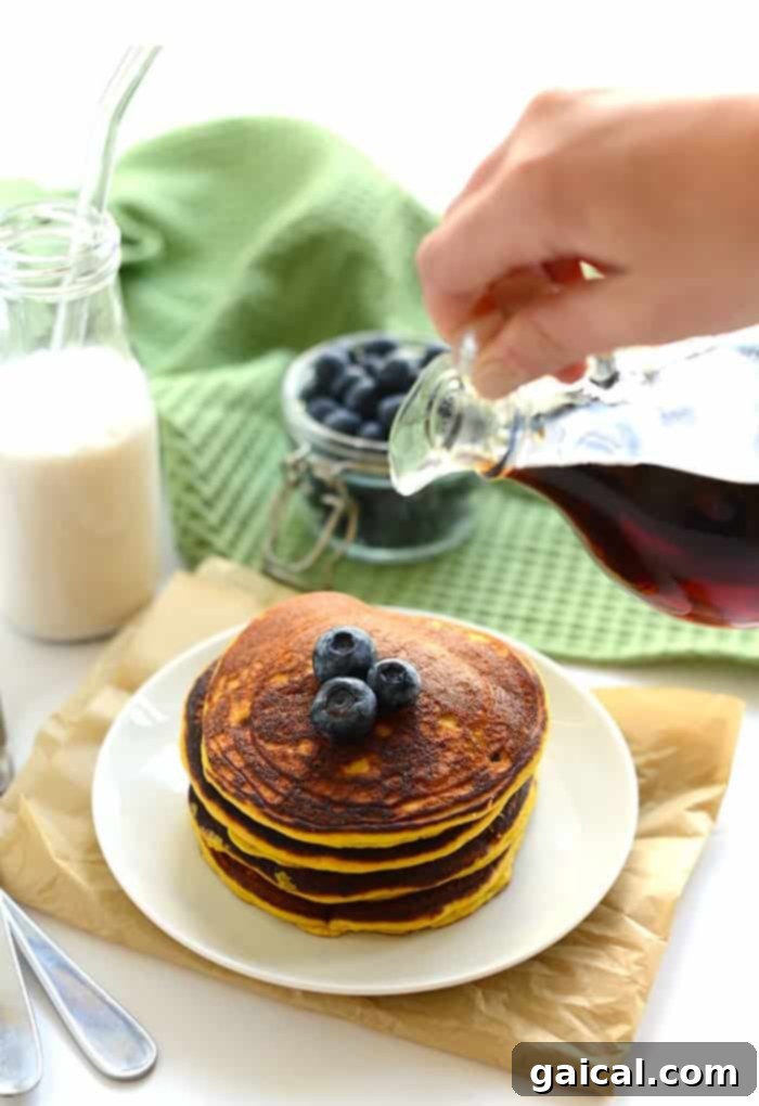 A stack of golden brown paleo coconut flour pancakes, garnished with fresh berries and a drizzle of maple syrup, ready to be enjoyed.
