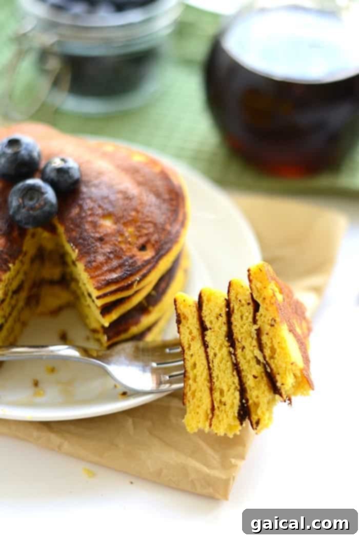 A fork piercing a stack of fluffy paleo coconut flour pancakes, showcasing their soft interior and ready-to-eat appeal.