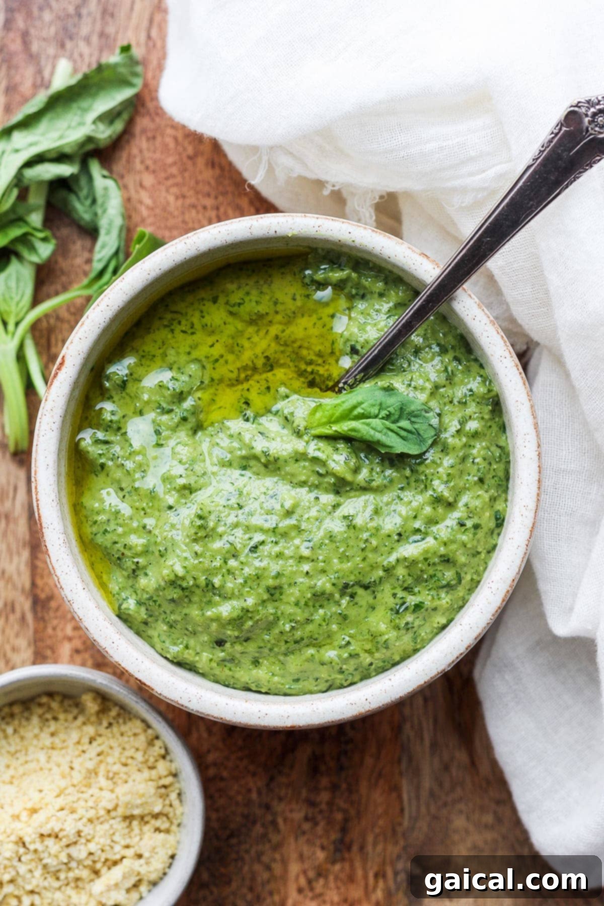 Vibrant green vegan pesto in a bowl with a spoon, garnished with fresh basil leaves.