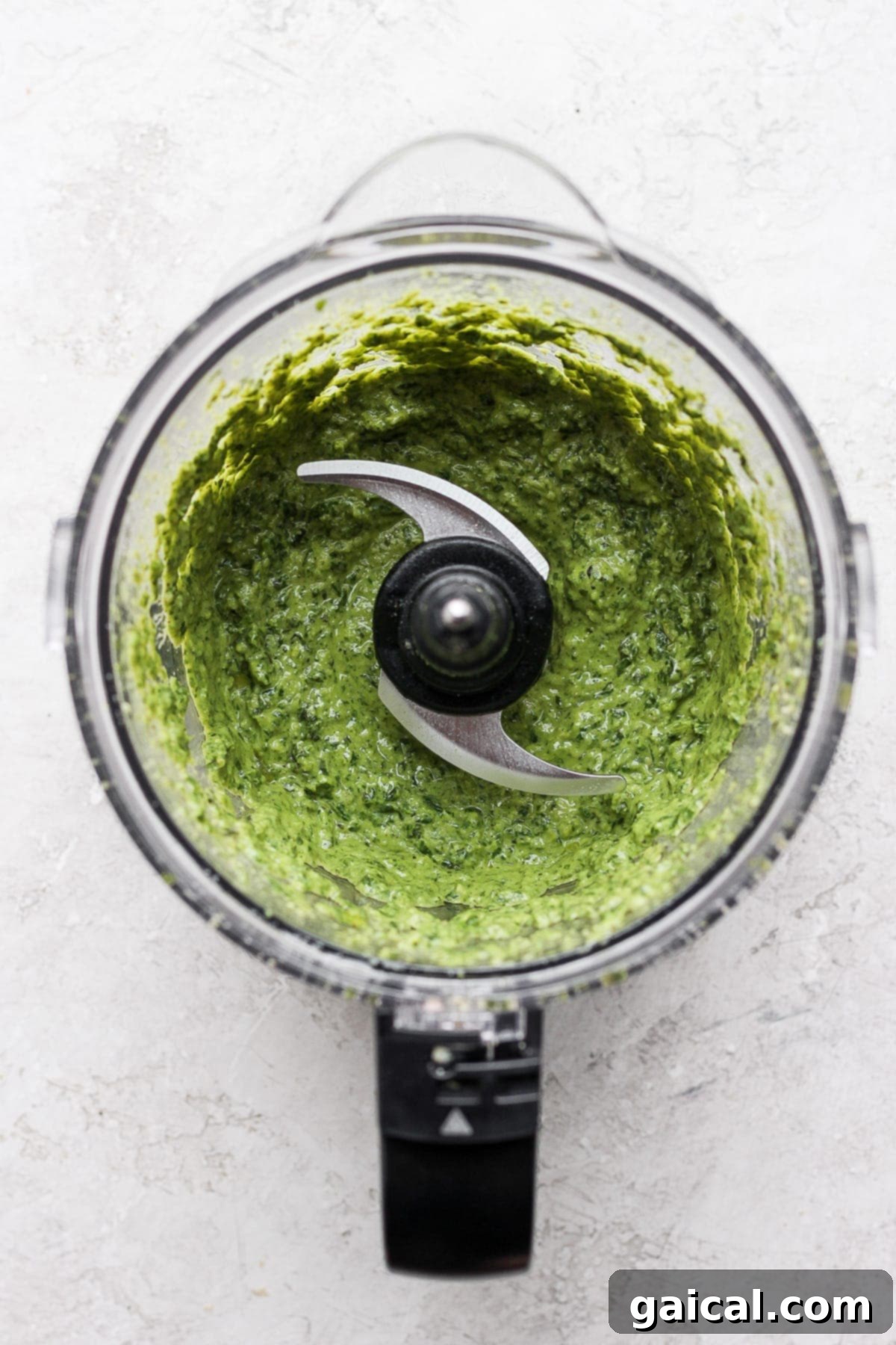 Smooth, green vegan pesto swirling inside a food processor bowl, ready to be scooped out.