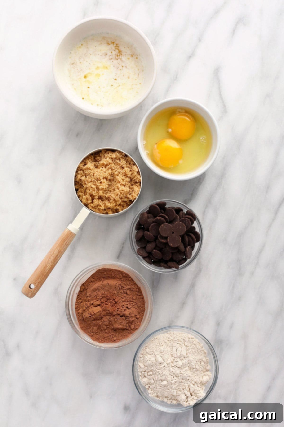 Ingredients for fudgy brownies: butter, eggs, brown sugar, chocolate chips, cocoa powder, and flour laid out