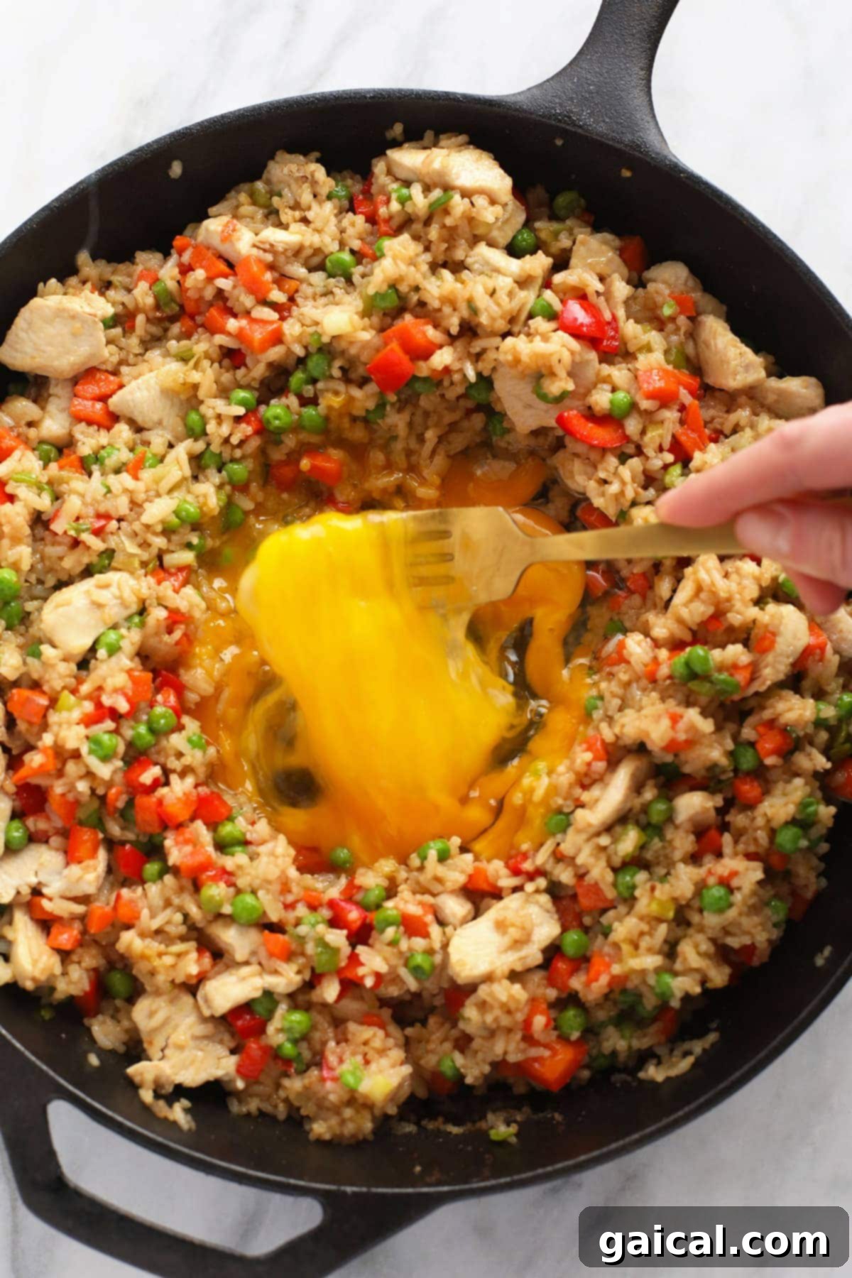Expertly scrambling eggs in the middle of a frying pan, surrounded by seasoned rice and vegetables.