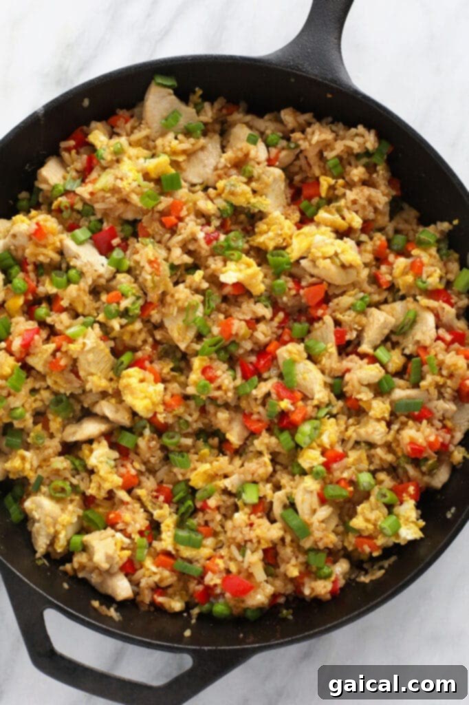Generous serving of chicken fried rice in a large cast iron pan, showcasing its rich colors and textures.