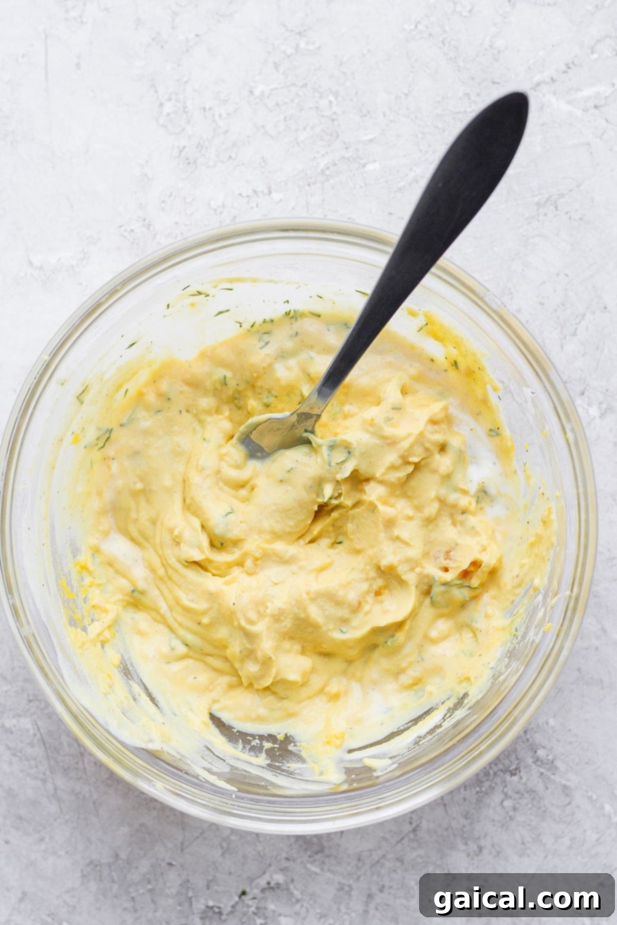 Mixing the perfectly creamy deviled egg filling. The creamy mixture of deviled egg filling being stirred with a spoon in a clear glass bowl, showcasing its smooth texture.