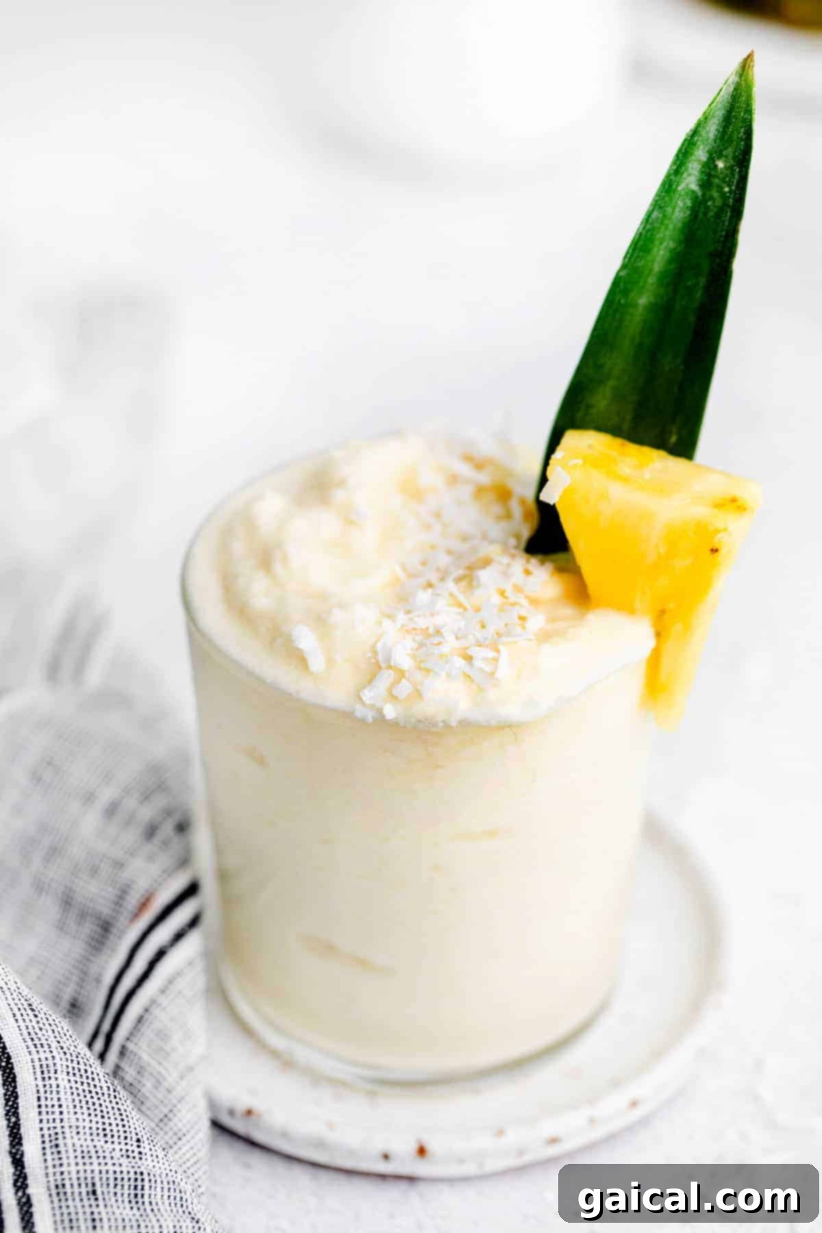 A refreshing Piña Colada in a tall glass, garnished with a frozen pineapple chunk and a tiny umbrella, against a soft, blurred background.