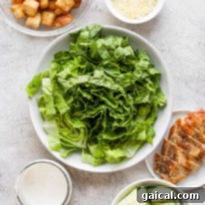 Ultimate Chicken Caesar 5 Various fresh ingredients for a chicken salad are arranged in a large bowl, ready for mixing.
