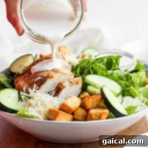 Ultimate Chicken Caesar 6 Caesar dressing is being poured over a fresh salad, ensuring every leaf is coated.